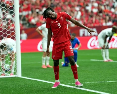 Johan Manzambi celebrates in a red Switzerland shirt near the goal with a tilted head gesture