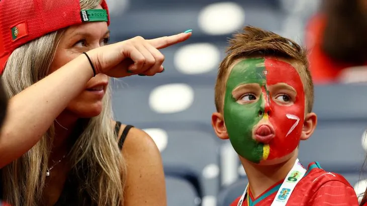 A woman points as she sits next to a child with his face coloured in the Portuguese flag.